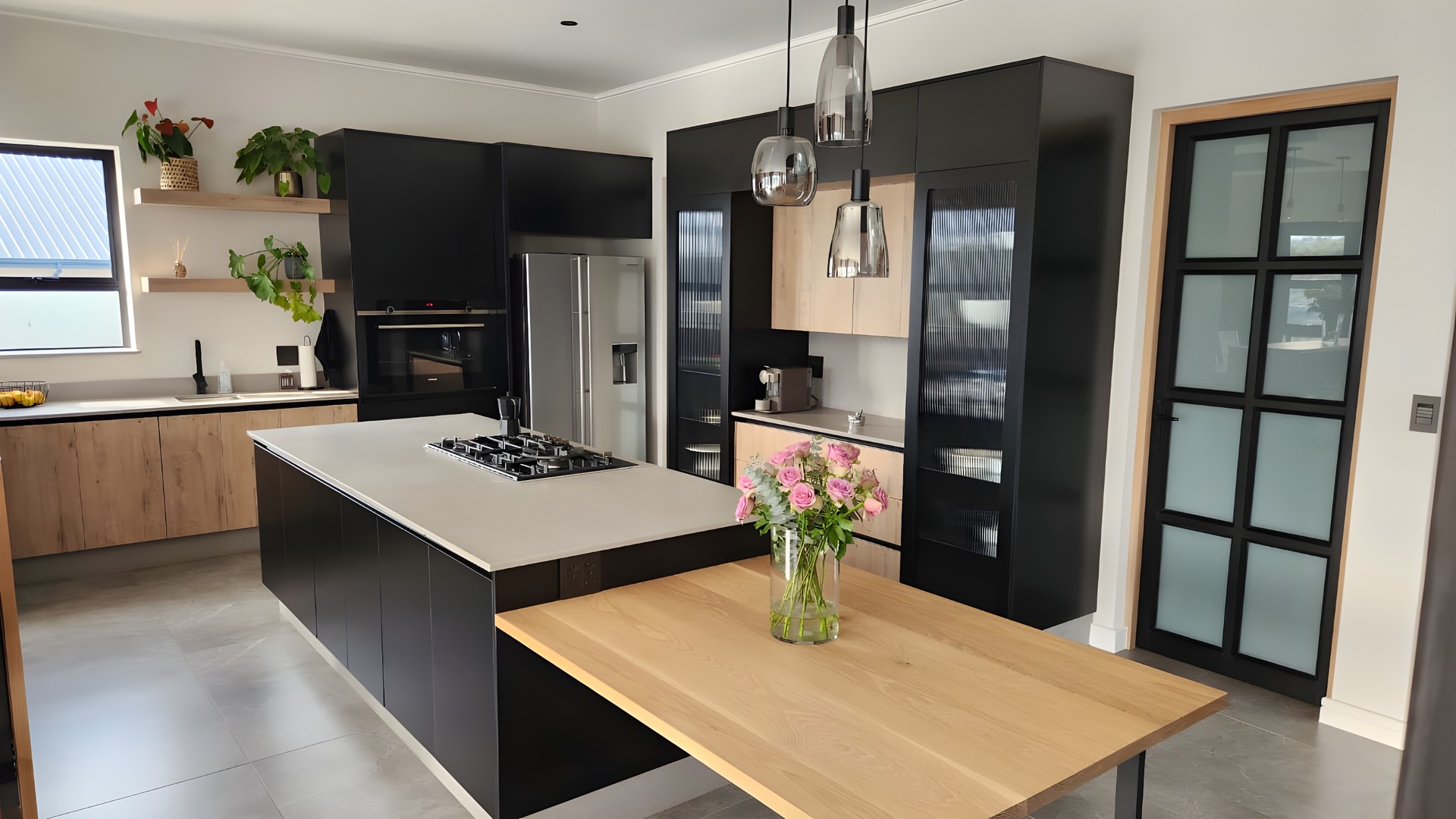 A dark, finely composed kitchen with matte black cabinetry, oak floating shelves and a stone island