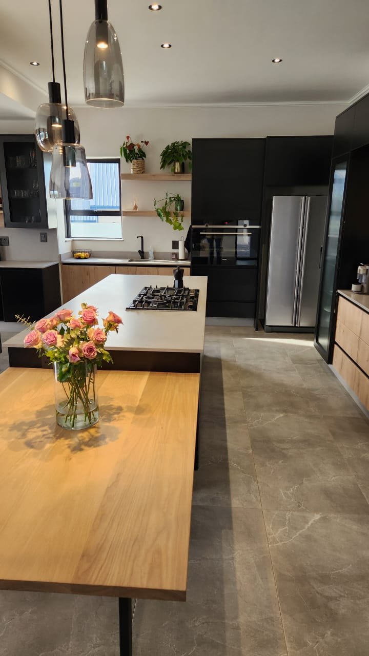 A dark kitchen with stone island, breakfast table with roses and stainless side-by-side fridge