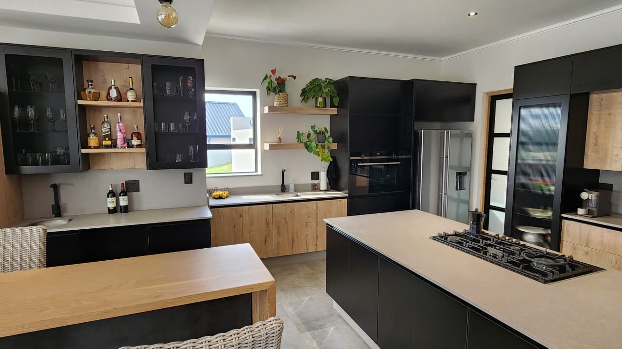A wide kitchen with black cabinetry, oak base units, illuminated bar display and a working pantry beyond