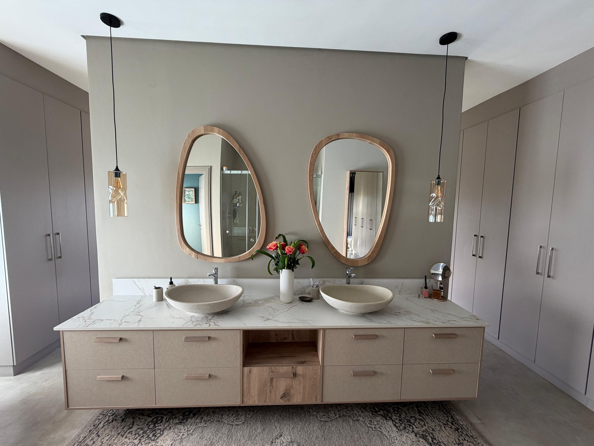 Premium bathroom with double stone basins, pebble-shaped oak mirrors, marble counter and flanking fitted wardrobes
