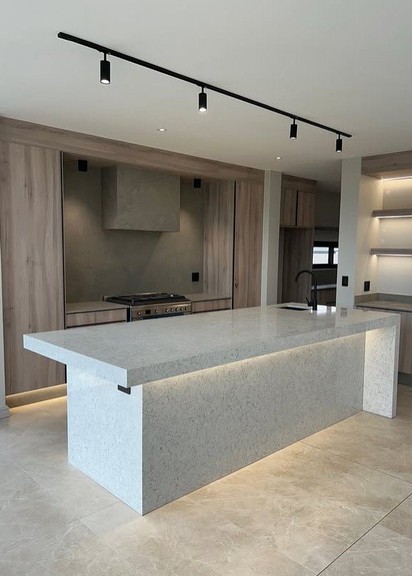 A modern Tamsa kitchen with wood-clad cabinetry, stone island and concealed lighting