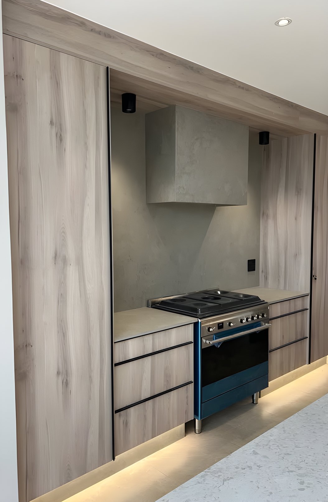 A bespoke Tamsa kitchen wall with wood-clad cabinetry, freestanding range and recessed plinth lighting