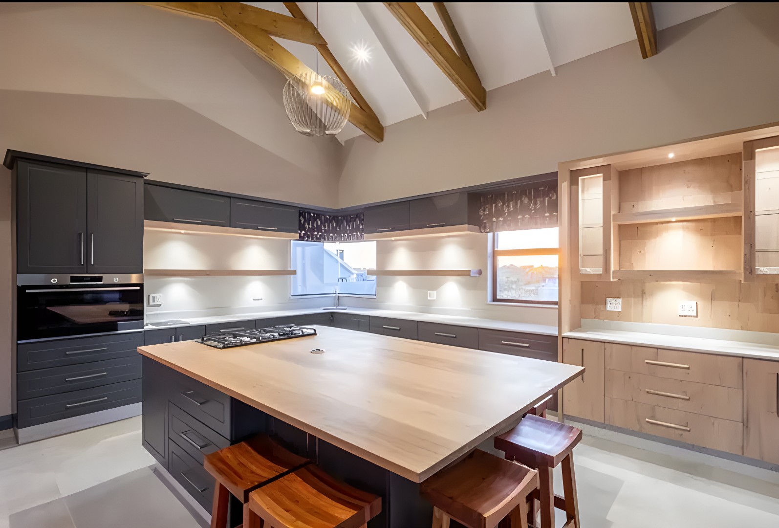 A contemporary kitchen with dark cabinetry, wood-clad island, exposed beams and a vaulted ceiling