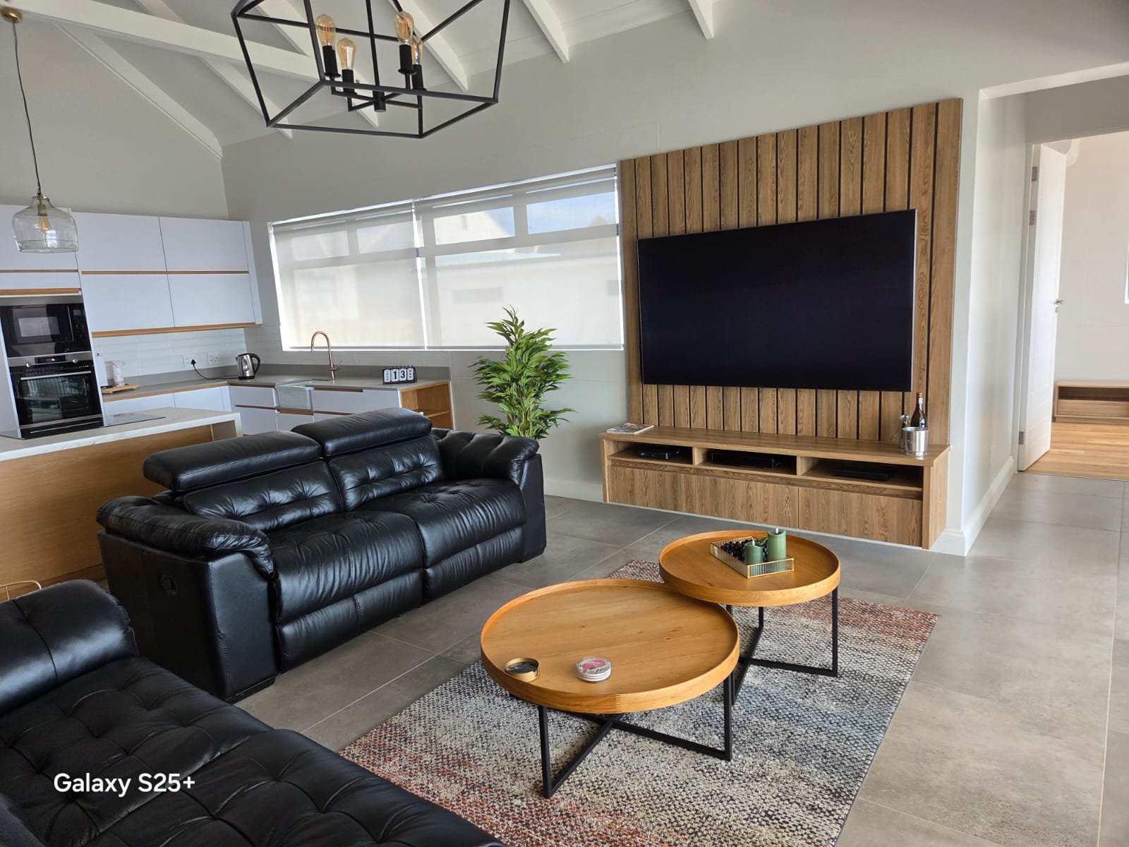 Open-plan living room with oak slat television wall, leather sofas and a pendant cluster